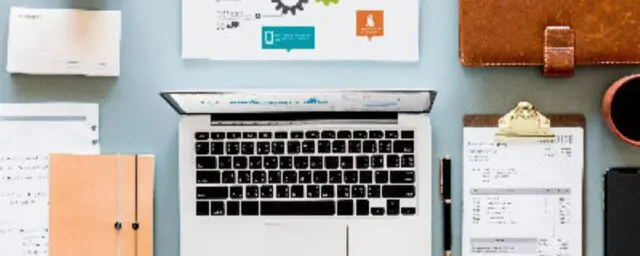 広告制作およびグラフィックデザイン事業の合併・買収（M&A）成約事例インタビューを紹介するメインビジュアル。机の上に配置されたノートパソコン、ノートブック、ペン、定規、クリップボードのイメージ写真