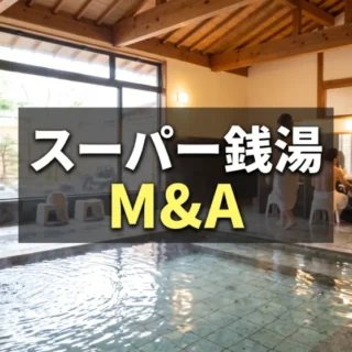 伝統的な木造建築のスーパー銭湯の屋内に、湯気が立ち上る広い温泉と洗い場があり、M&Aの文字が中央に配置された画像。