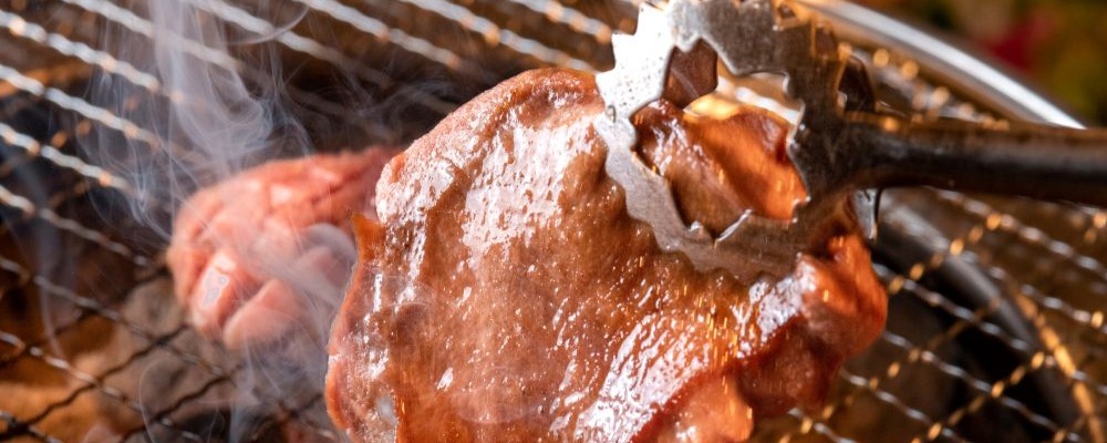 網の上でジューシーに焼かれている焼肉（N社さまの焼肉チェーン運営事業譲渡のイメージ）
